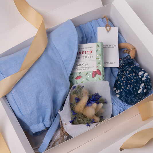 Baby boy or girl gift box in beautiful powder blue organic linen, including baby bloomer and bonnet / sunhat, hair, natural wooden teether and dried flower posy bouquet. Bennetto Chocolate for new mum.