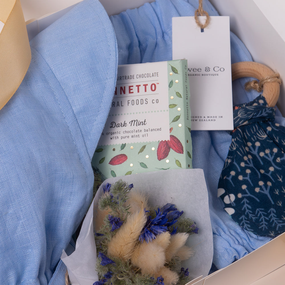 Baby boy or girl gift box in beautiful powder blue organic linen, including baby bloomer and bonnet / sunhat, hair, natural wooden teether and dried flower posy bouquet. Bennetto Chocolate for new mum.