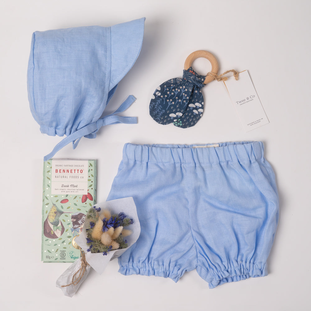 Baby boy or girl gift box in beautiful powder blue organic linen, including baby bloomer and bonnet / sunhat, hair, natural wooden teether and dried flower posy bouquet. Bennetto Chocolate for new mum.