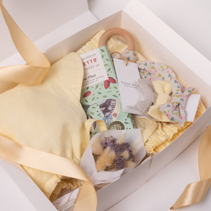 Baby boy or girl gift box in beautiful buttercup lemon organic linen, including baby bloomer and bonnet / sunhat, hair bows, natural wooden teether and dried flower posy bouquet. Bennetto Chocolate for new mum.