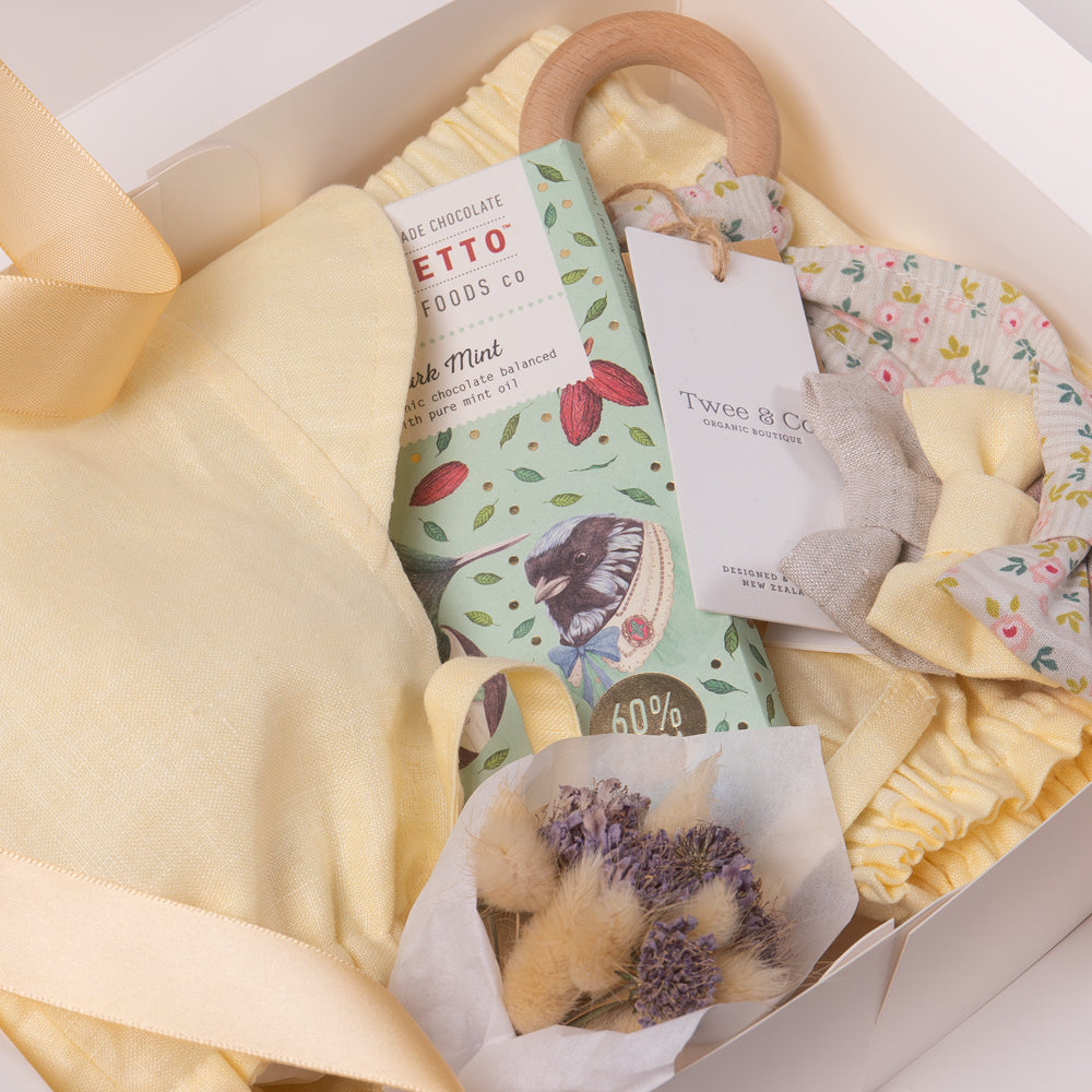 Baby boy or girl gift box in beautiful buttercup lemon organic linen, including baby bloomer and bonnet / sunhat, hair bows, natural wooden teether and dried flower posy bouquet. Bennetto Chocolate for new mum.