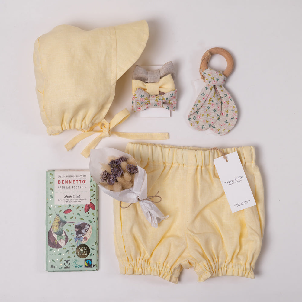 Baby boy or girl gift box in beautiful buttercup lemon organic linen, including baby bloomer and bonnet / sunhat, hair bows, natural wooden teether and dried flower posy bouquet. Bennetto Chocolate for new mum.