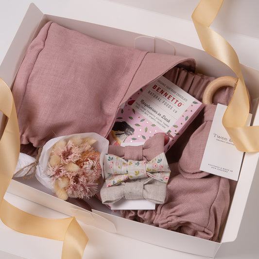 Baby girl gift box in beautiful vintage rose organic linen, including baby girl bloomer and bonnet / sunhat, bow hair ties, natural wooden teether and dried flower posy bouquet. Bennetto Chocolate for new mum.